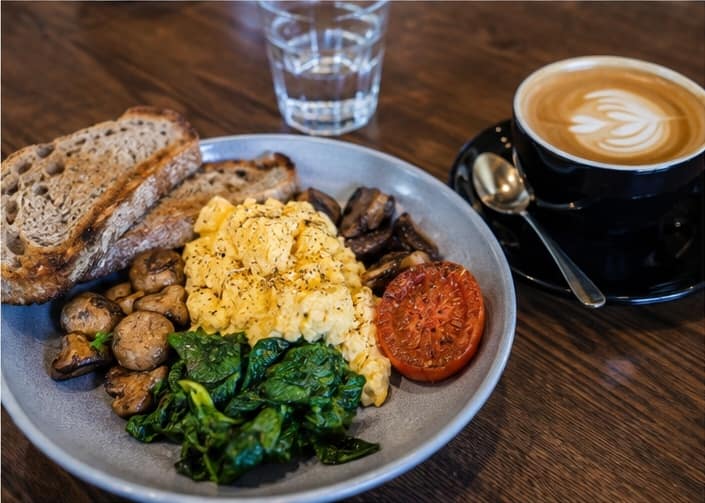 Fresh breakfast plate with scrambled eggs, mushrooms, spinach, toast and coffee at a South Australian cafe